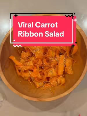 The cover image features a wooden bowl filled with a vibrant carrot ribbon salad. The salad is composed of orange carrot ribbons with sprinkled sesame seeds. The salad is in the center of the frame, against a neutral, light-colored background. The top of the image has a red rectangle with a white border, containing the text 'Viral Carrot Ribbon Salad'.