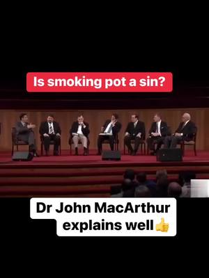 The cover image shows a panel discussion. Seven men in suits are seated on a stage with a dark background. Above them is a red banner with white text, and below the stage are the heads of audience members. A white box with text appears at the bottom of the image.
