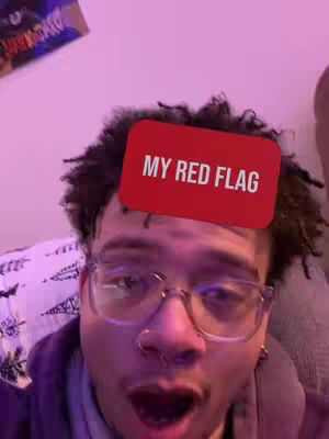 A selfie with a man in glasses looking at the camera with a shocked expression. He has a red square with white text overlayed on his forehead, and the background is a soft pink with a glimpse of a poster.