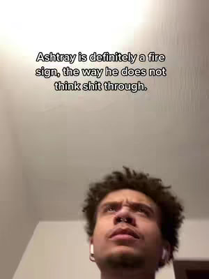 A dimly lit selfie-style shot features a young man with curly hair, positioned from the chest up. He wears a nose ring and earbuds, with a slightly furrowed brow and his eyes directed upwards, suggesting contemplation. Above him, text overlays appear. The background is a plain wall.