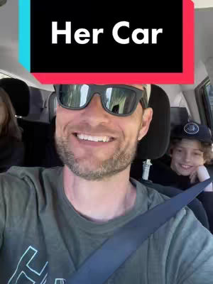 A man with sunglasses in the driver's seat of a car smiles at the camera, a child sits in the back and smiles, while there is a text overlay at the top.
