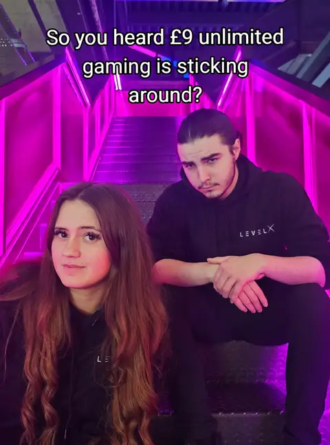 The cover image features two people, a woman and a man, seated on a staircase in a location with bright pink and purple lights. The woman is in the foreground, facing the camera with long brown hair and wearing a black hoodie. The man, positioned slightly behind her, is also wearing a black hoodie, with his hair pulled back and a thoughtful expression. Above the woman, a text overlay reads, 'So you heard £9 unlimited gaming is sticking around?'