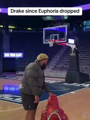Image shows a man on a basketball court, leaning toward a pair of red and white sneakers. The court has a wooden floor with blue lines and a basketball hoop in the background with some stadium seating.