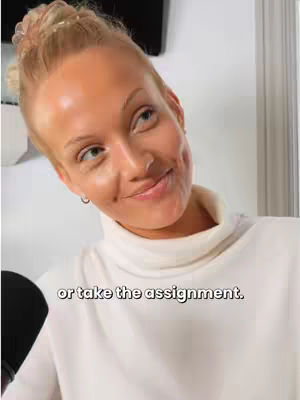 A woman with blonde hair and a white turtleneck smiles, angled slightly to the side. The text overlay is visible at the bottom of the frame. The background is blurred, but seems to be an indoor setting.