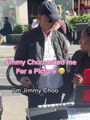 An image shows a man in a black cap and jacket with a white shirt. He is looking down and to his side. The text overlay reads, "Jimmy Choo asked me For a Picture 😊 I'm Jimmy Choo". A woman is standing to the right of the man. The setting appears to be outdoors near a city street.