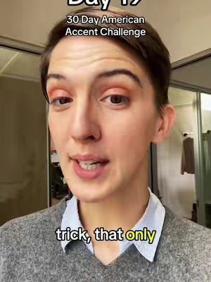 A woman looks directly at the camera, speaking. Text overlays the image, including "Day 19" and "30 Day American Accent Challenge" at the top, and "trick, that only" near the bottom. The background is a blurred interior with reflective surfaces and a coat.