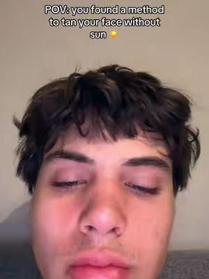 A close-up selfie of a young man with dark hair and closed eyes. Text overlayed at the top says: POV: you found a method to tan your face without sun.
