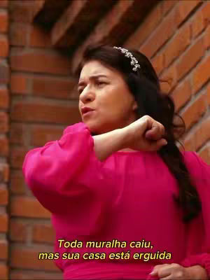 A woman in a pink dress is leaning against a brick wall, with the camera focused on her upper body. She appears to be deep in thought or speaking passionately, with a text overlay at the bottom.