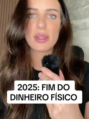 A woman with dark hair is holding a microphone and speaking. The image has a text overlay that reads "2025: FIM DO DINHEIRO FÍSICO." The background is a blurred, neutral-toned wall, and the woman is wearing a black top.