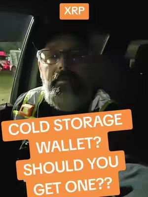 A man wearing glasses and a safety vest is sitting in a car and addressing the camera.  Above his head, there's an orange box labeled "XRP". In the foreground, a series of overlapping, orange rectangles spell out, in white font, the questions, "COLD STORAGE WALLET? SHOULD YOU GET ONE??"