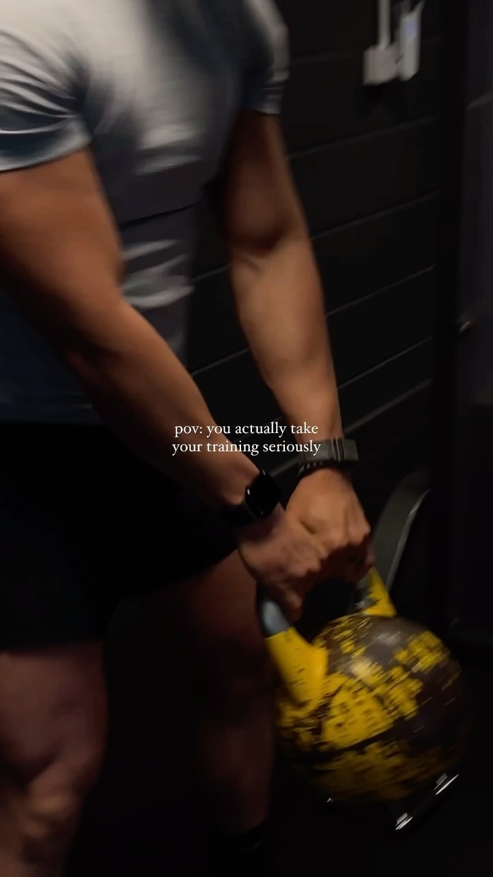 A person is holding a yellow kettlebell in a dimly lit gym. The focus is on the person's arms and the kettlebell, with the text overlayed.