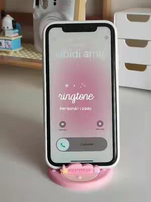 The cover image shows an iPhone displaying a customized ringtone on its screen. The phone rests on a pink phone holder. The background includes other items like a desk and a small white cabinet.
