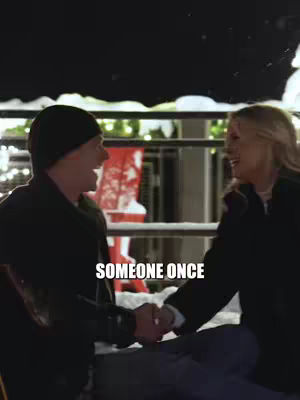 A romantic cover image showing a man and a woman holding hands. They are holding hands and looking into each other's eyes, with visible amusement. The scene appears to be set outdoors during winter, with snow and Christmas lights in the background.