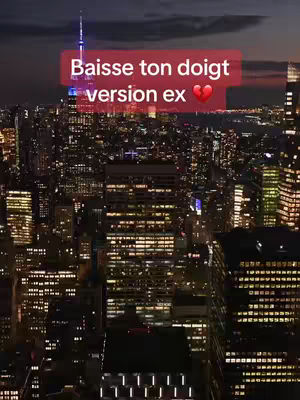 An aerial view of a city at night, with numerous illuminated buildings creating a grid-like pattern. The sky is a deep, dusky color. A red rectangle with white text reading "Baisse ton doigt version ex" is overlaid on the image. A heart icon is also included in the rectangle.