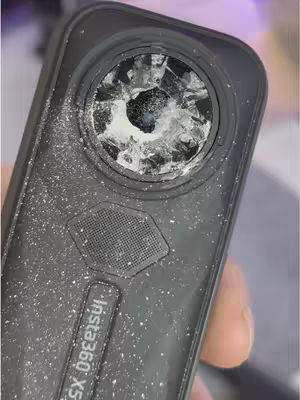 The cover image displays a close-up of a black camera, likely an action camera, with a shattered lens. The lens is circular and the damage shows a starburst pattern of cracks and breaks, indicating a significant impact. Small white particles, possibly from the shattered glass or the environment, are scattered across the camera body. The camera has the 'insta360 X5' branding on it, with other details like a small speaker-holed design. The lighting appears bright and highlights the texture of the camera body and the broken lens. The overall composition is focused on the damage, suggesting a possible issue or comparison.