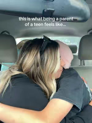 The image shows a woman embracing another person inside a car. The woman has long blonde hair and is wearing a black shirt. The other person is wearing a pink hoodie. The text overlay at the top reads "this is what being a parent of a teen feels like..."