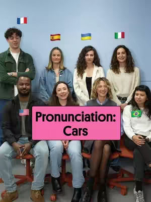 A cover image with a group of people of diverse backgrounds, all seated on chairs. A pink sign displays the words 'Pronunciation: Cars' in dark text. Above the individuals, several flags are present, representing various countries, implying a language or international theme. The background is a solid blue wall.