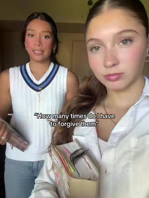 Two young women are positioned in a scene. One is in the foreground, partially cropped, with light skin, long brown hair pulled back, and a white button-up shirt. The other woman is in the background, facing slightly to the side, with a darker complexion, dark hair, a white sleeveless top, and blue jeans. A text overlay reads: 'How many times do I have to forgive them.'
