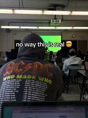 The cover image shows the back of a person wearing a black AC/DC band hoodie in a classroom setting. The classroom has rows of desks, a bright green projection screen, and fluorescent lighting. A text overlay reads, 'no way this is real' with an emoji indicating a surprised expression.