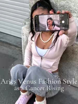 A woman is holding a phone up in front of her face, with the phone displaying a photo and text overlayed. She is wearing a pink zip-up hoodie, blue jeans, and pink shoes. She has a pearl necklace on, and her black hair is pulled back in a ponytail. Text on the phone screen shows another image of the woman. The backdrop is a concrete surface and a white slatted wall. The title text is arranged below, partially obscuring the person's midsection.