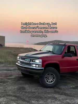 A red pickup truck is parked on a dirt road with a sunset in the background and some text on the top.