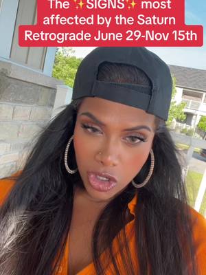 A woman in an orange shirt and black cap is looking at the camera with her tongue out. Text overlayed in the top of the image is "The ✨SIGNS✨ most affected by the Saturn Retrograde June 29-Nov 15th". The background appears to be a house entrance.
