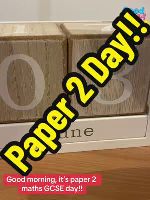 The cover image shows a wooden block calendar displaying '03' with the word 'June' visible. Overlaid on the image is a yellow and black text graphic that reads 'Paper 2 Day!!'. Below this, a red banner with white text says, 'Good morning, it's paper 2 maths GCSE day!!'. The blocks sit on a light brown wooden surface.