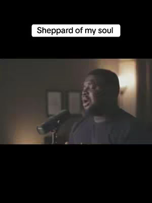 A man is singing into a microphone, set against a dimly lit background. Above him, a text overlay reads 'Sheppard of my soul'. The image has a professional, moody aesthetic.