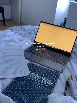 A medium shot shows a laptop on a bed. A notebook, papers, and colorful pens are arranged near the laptop. The text overlay conveys the video's topic.