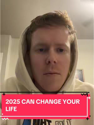 A man with fair skin and reddish hair is centered in the frame, wearing a cream-colored hoodie. Behind him, a plain wall and a portion of a framed picture are visible. A red bar overlay at the bottom states "2025 CAN CHANGE YOUR LIFE".