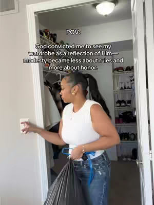 A woman is standing with her back to a closet, holding a garment bag and wearing a white top and jeans. Text overlays the image.