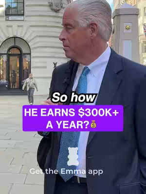 A medium shot of a man in a suit and tie, standing outside a building. A purple bar with white text overlays his chest, and a small gummy bear icon is at the bottom. In the background, there's a classic building facade and another person walking away.