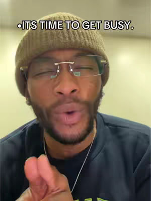 A man with a brown beanie and glasses is shown from the chest up, delivering a message with a raised finger. Text overlays the image.