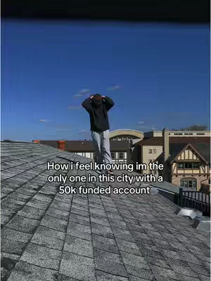 A man in a black hoodie and grey pants stands on a dark grey roof, hands on his head, looking out over a cityscape. The sky is a clear, vibrant blue, and various buildings with different architectural styles form the background. Text overlaid mentions a 50k funded account.