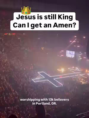 The image shows a wide shot of a large venue, likely a concert or event, filled with a crowd. A large cross made of lights is prominently featured on the floor, suggesting a religious theme. Above, text overlay with a crown graphic reads “Jesus is still King / Can I get an Amen?”. The overall composition is colorful with lights, capturing the atmosphere of the event.