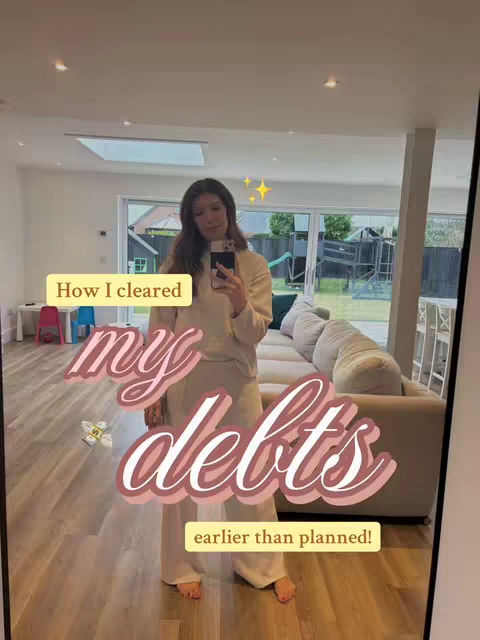 A woman in a beige outfit is taking a mirror selfie in what appears to be her home, showing a clean, well-lit interior and a glimpse of the outdoors through large windows. A text overlay on the mirror reads "How I cleared my debts earlier than planned!" with a cartoon money graphic.