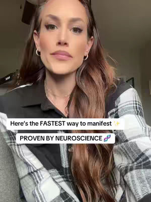 A woman with long brown hair is the main focus, looking directly at the camera with a neutral expression. She is wearing a black and white checkered shirt and small hoop earrings with visible makeup. The background is blurred, with hints of a room visible. A text overlay with the text 'Here's the FASTEST way to manifest' is present.