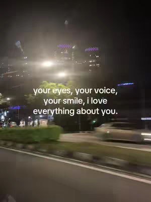 A nighttime scene viewed from a moving vehicle, with blurred lights, buildings and a visible road. Text overlayed on the image.
