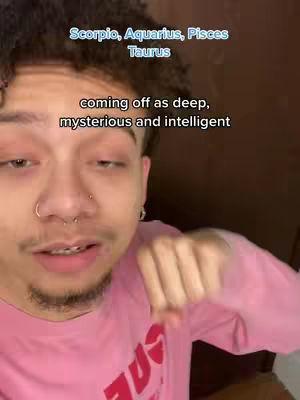 A young man with curly hair and facial piercings looks toward the camera, the top half of his body is visible. Text overlays in light blue and black state 'Scorpio, Aquarius, Pisces, Taurus' and 'coming off as deep, mysterious and intelligent.' The man wears a pink shirt.