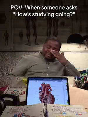 A man is seemingly crying while studying, with a tablet displaying a diagram of a heart and notes laid out on a table, as well as an open notebook. The text overlay reads 'POV: When someone asks "How's studying going?"'