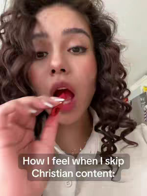A close-up shot of a light-skinned woman looking at the camera, with partly open mouth and a red candy pulled towards her mouth. Her dark curly hair frames her face, enhanced with makeup. A text box overlays the bottom, reading: How I feel when I skip Christian content:.
