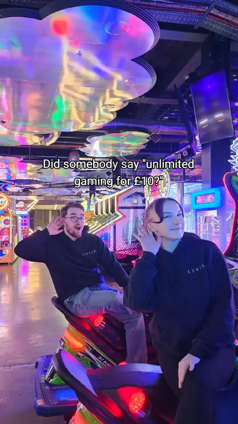 Two people are in an arcade, with a man in the foreground leaning towards the camera and the woman with her hand on the right. Text overlay is on top stating, 'Did somebody say "unlimited gaming for £10?"'