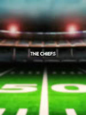 The image shows a football field perspective, with green grass marked with white lines. The text "THE CHIEFS" is centered. The background is a blurred stadium with lights.