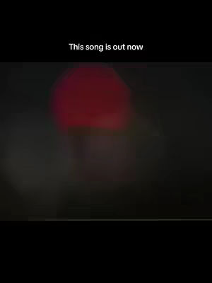 The cover image is a vertical shot with a blurred background. At the top is a text overlay that reads "This song is out now." The primary visual element is a large, indistinct red shape, possibly a spotlight or a blurry object, centered in the frame. The rest of the image is underexposed, making everything appear dark. Overall the composition is simple and atmospheric.