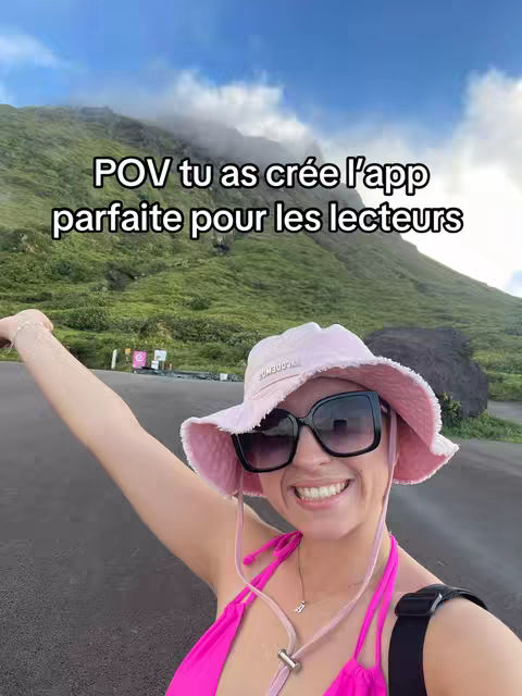 A woman wearing a pink sun hat and sunglasses stands with one arm raised in the air. She is smiling, and a scenic background of a green mountain and blue sky is visible.
