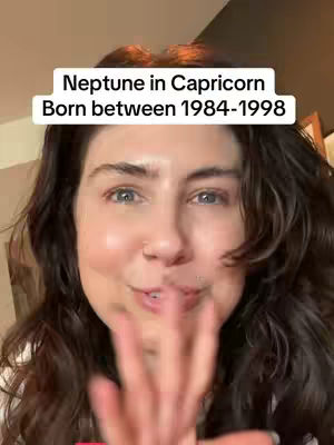 A woman with long, dark hair is centered in the frame, smiling and gesturing with her hand towards the camera. A text overlay in a white box reads, "Neptune in Capricorn Born between 1984-1998