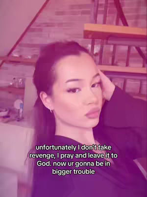 The cover image showcases a young woman with dark hair. She is looking towards the camera with a slight pout, and her hand is close to her head. The background is blurred, with a combination of pink and purple hues, and a suggestion of a wooden structure. Text overlayed on the image reads:  "unfortunately I don't take revenge, I pray and leave it to God. now ur gonna be in bigger trouble".