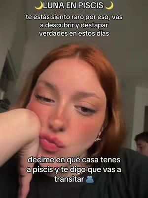 A woman with red hair is the focus of the image, with text overlays informing the viewer about astrological insights. The woman has fair skin and is looking towards the right side of the frame with light makeup, including blush and lipstick. She has one hand resting against her cheek. Behind her is a blurred background with other people.