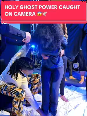 A video cover presents a scene from what appears to be a religious event. A woman stands amidst a group of people, with several individuals touching her, presumably as part of a ritual. Text overlayed on the image reads 'HOLY GHOST POWER CAUGHT ON CAMERA,' indicating the video's subject. The color scheme is dominated by cooler tones: blue background, with a group of people