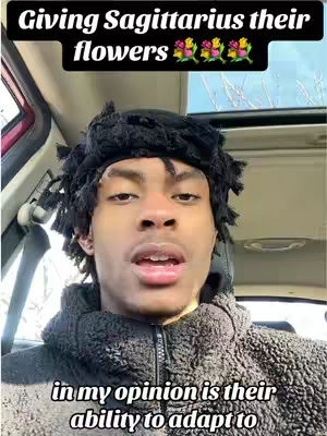 A selfie-style shot of a young man in a car. The man has short dreadlocks with a band around his forehead and a dark-colored fleece jacket. He is facing the camera with his mouth slightly open. Above him is a black banner with white text and three rows of colorful flower emojis.